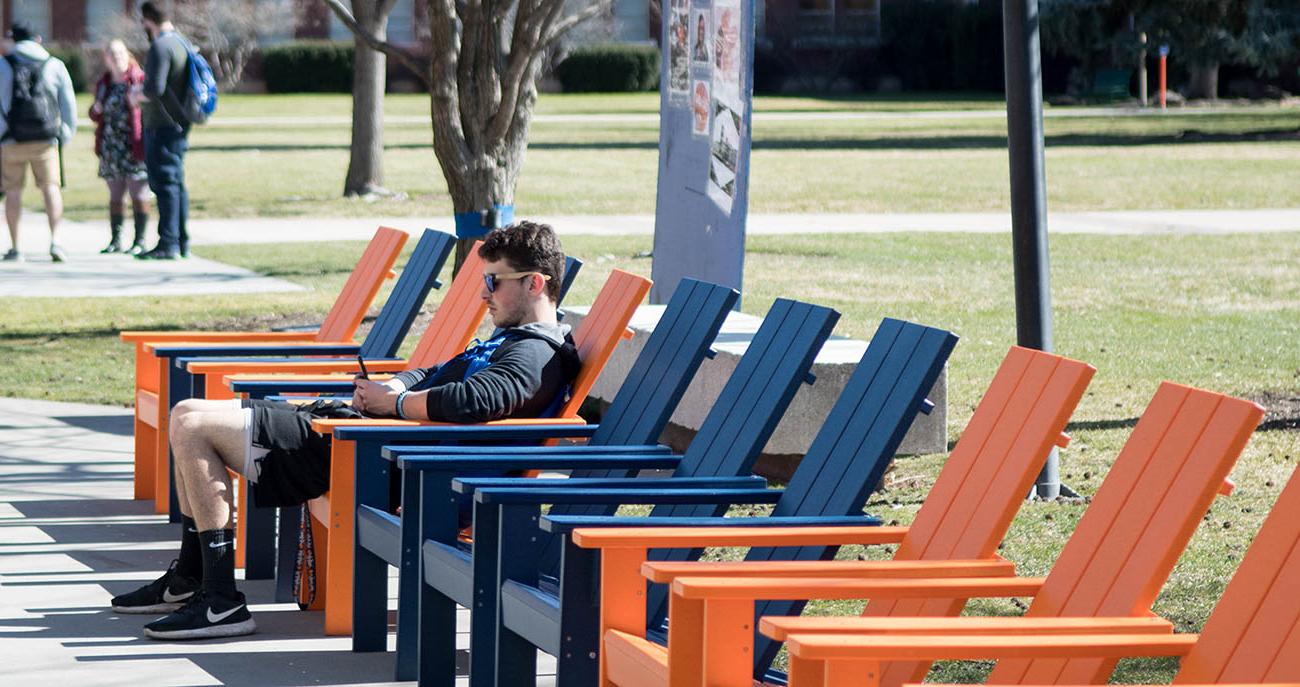 Student sitting outside in a chair, using his phone.